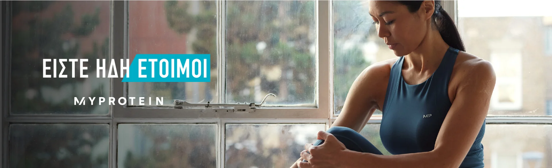 A woman wearing MP gym clothing sat on a window ledge stretching with the text 'You're Already Ready - MYPROTEIN' overlaying the image.
